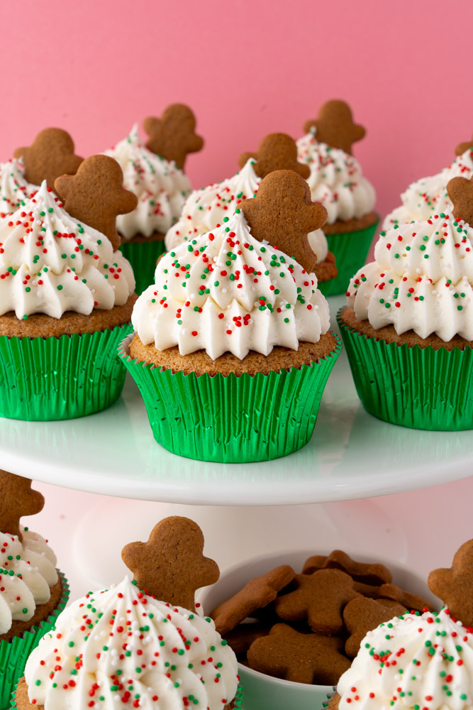Gingerbread cupcakes with cream cheese frosting and holiday sprinkles on a white cake stand.