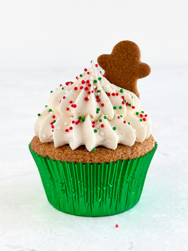 Gingerbread cupcake frosted with cream cheese frosting and decorated with holiday sprinkles and mini gingerbread men.