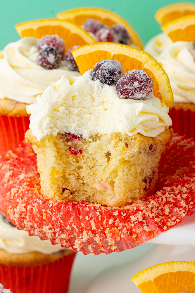 Orange cranberry cupcake with a bite taken out to show the texture of the cake and frosting.