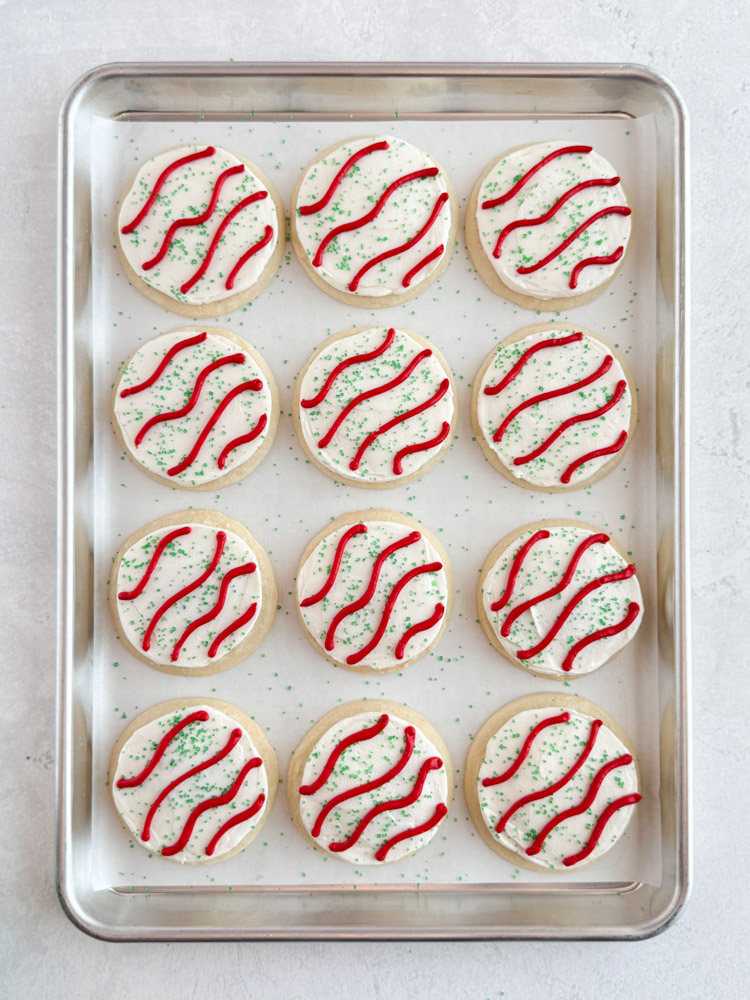 Vanilla cookies frosted with vanilla buttercream frosting decorated with green sanding sugar and stripes of red buttercream frosting.