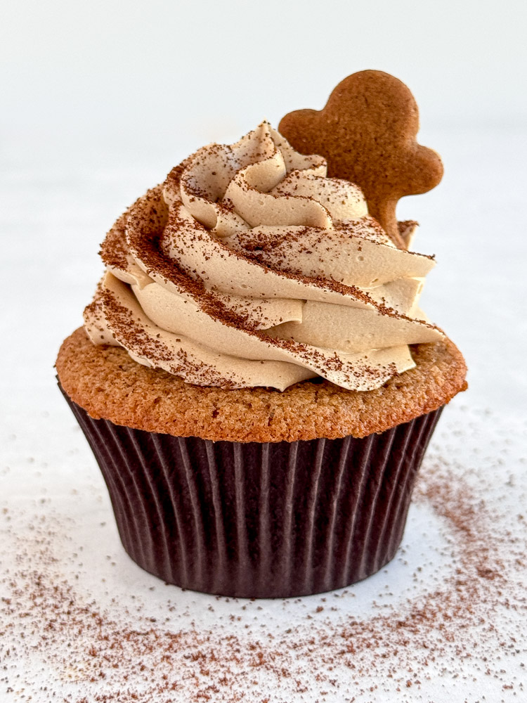 A decorated gingerbread latte cupcake with coffee buttercream, instant espresso powder dusting, and a mini gingerbread man.