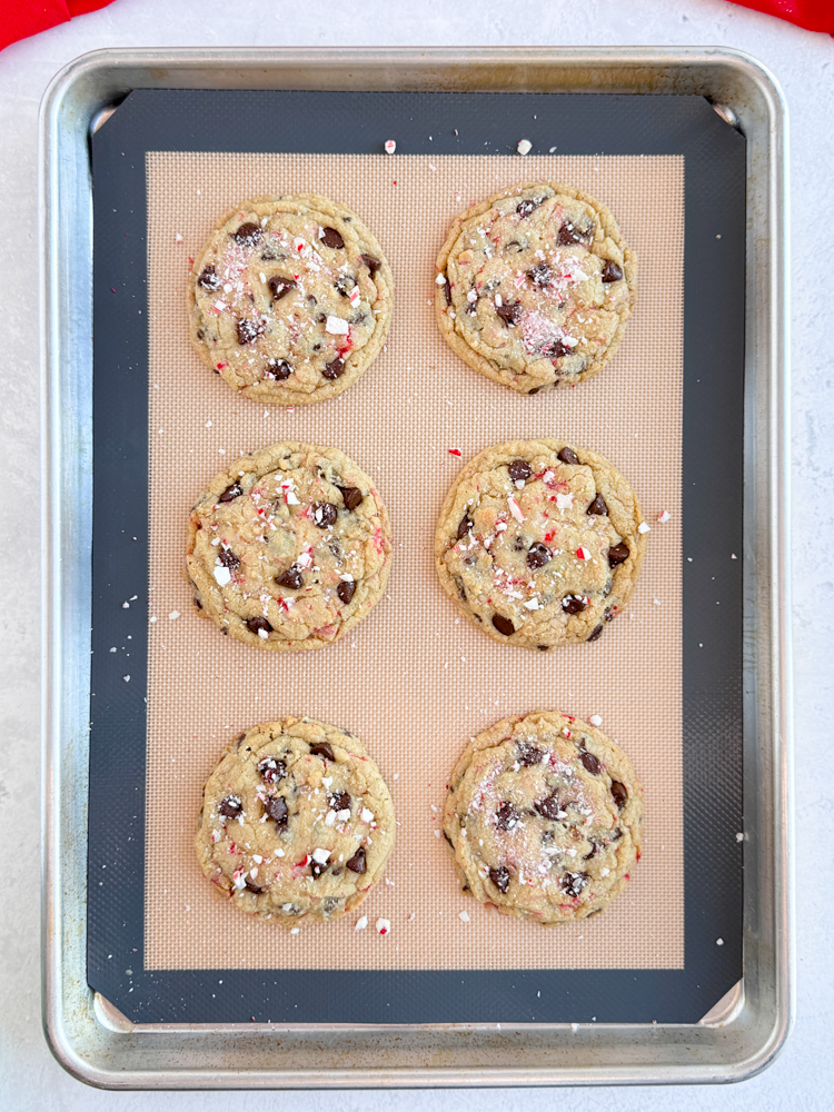 Baked peppermint chocolate chip cookies on a baking pan with crushed candy canes on top.