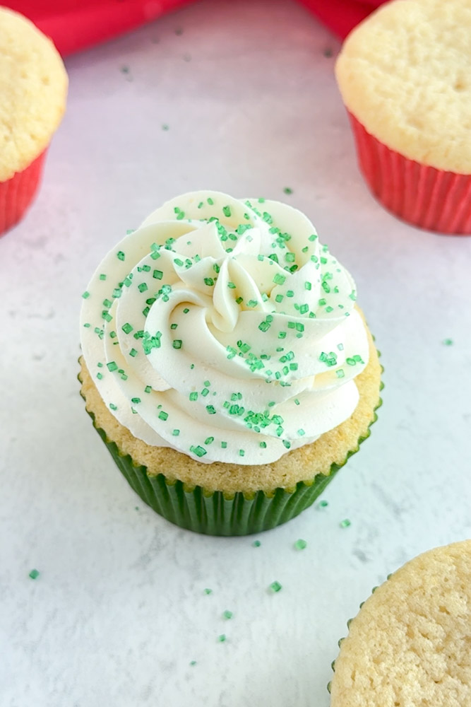 A vanilla cupcake frosted with vanilla buttercream frosting and decorated with green sanding sugar.