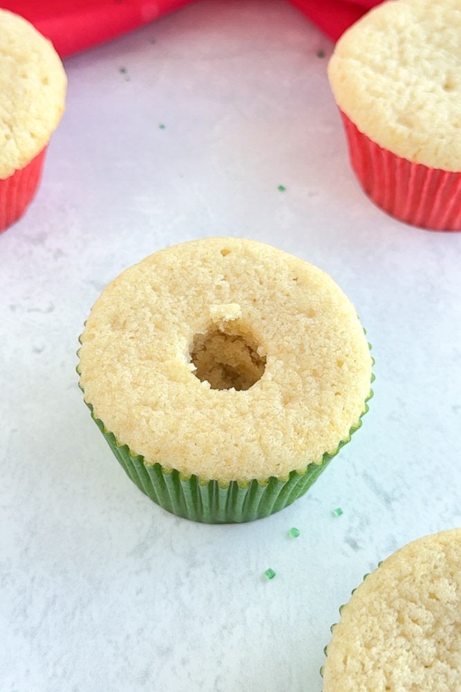 A vanilla cupcake with the center of the cake removed to create a hole.