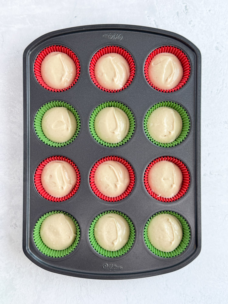 Vanilla cupcake batter in red and green cupcake liners in a cupcake pan.