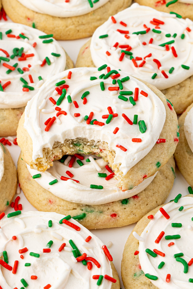 Christmas sugar cookies with vanilla frosting and sprinkles with a bite out of the cookie to show the chewy texture.