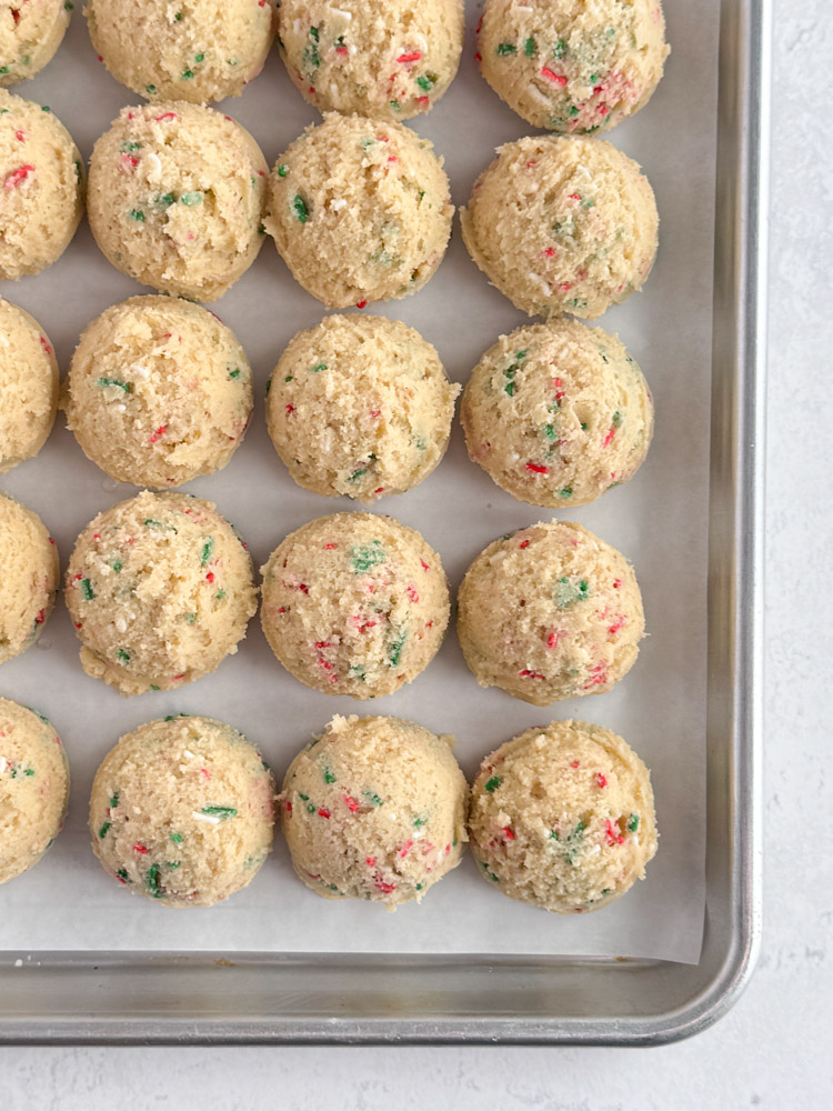 Sugar cookie dough balls on a parchment-lined baking sheet pan.