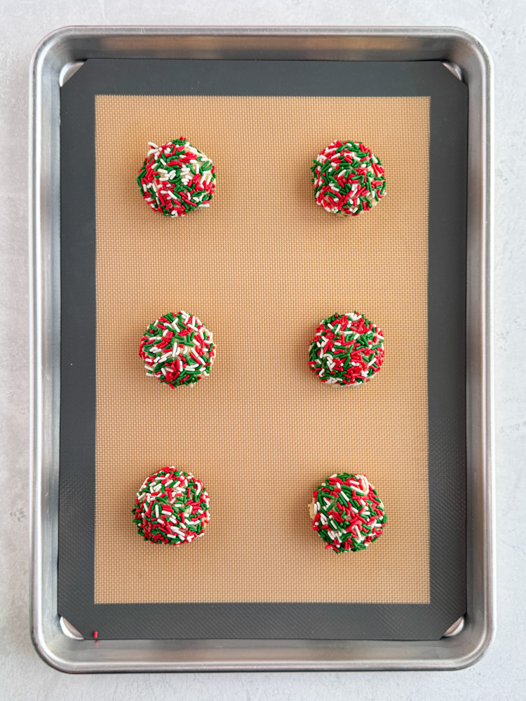 Sprinkle covered cookie dough balls on a baking sheet pan.