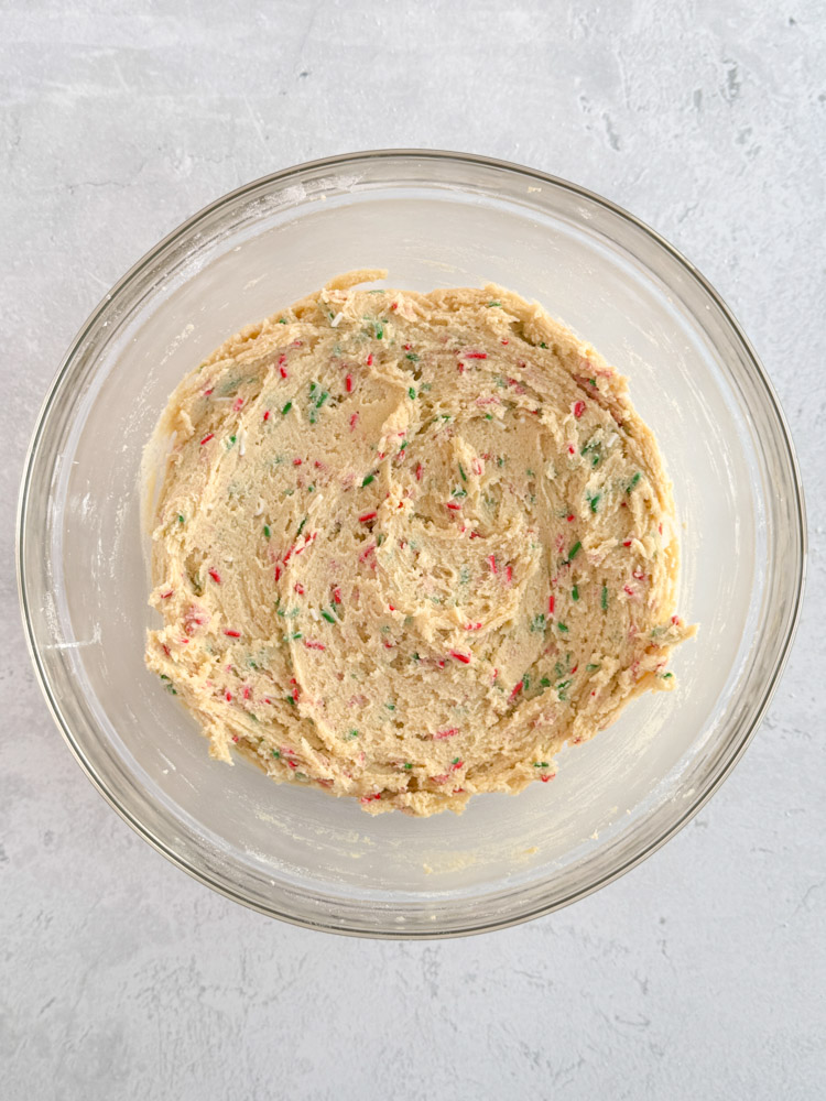 Vanilla sugar cookie dough with red, white, and green sprinkles in a mixing bowl.