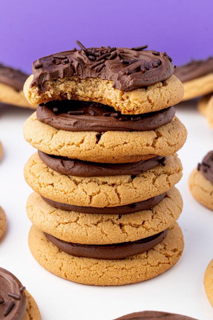 A stack of peanut butter cookies frosted with chocolate buttercream with a bite out of the top cookie to show the interior.