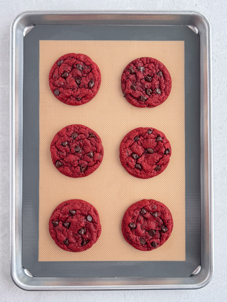 Baked red velvet chocolate chip cookies on a baking sheet pan.