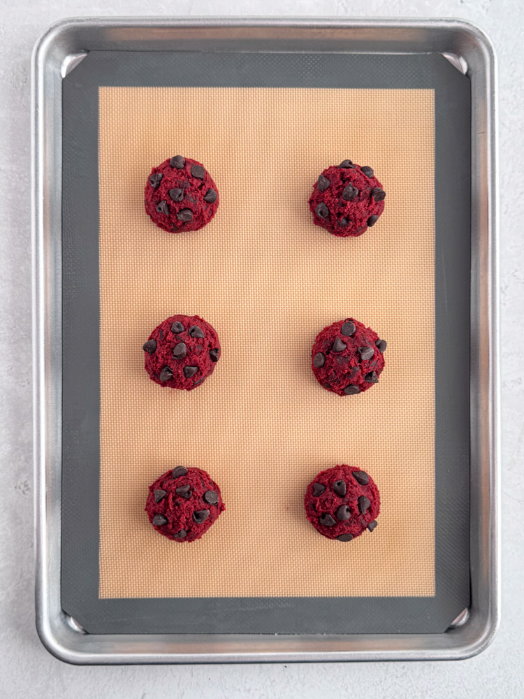 Cookie dough balls on a baking sheet pan with additional chocolate chips pressed into the dough.