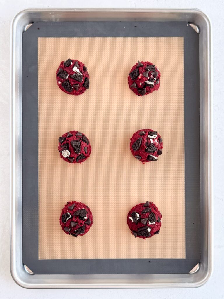 Cookie dough balls with chocolate chips and Oreo cookies on a baking sheet pan.