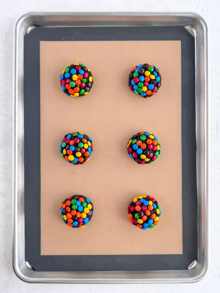M&M coated cookie dough balls on a baking sheet pan.