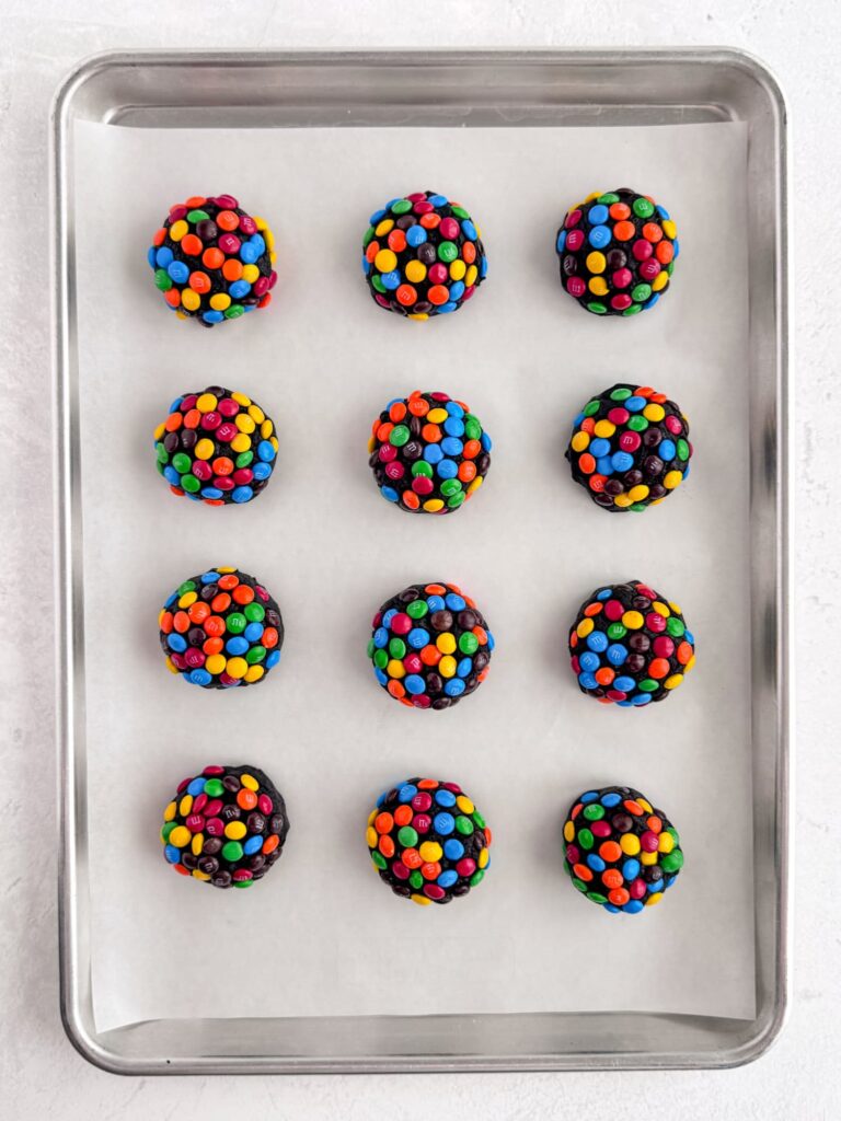 M&M covered cookie dough on a parchment-lined baking pan.