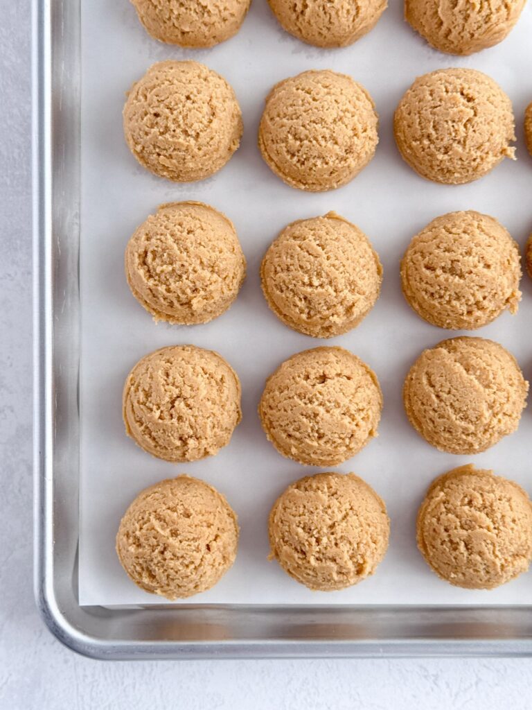 Cookie dough balls on a parchment-lined baking sheet pan.