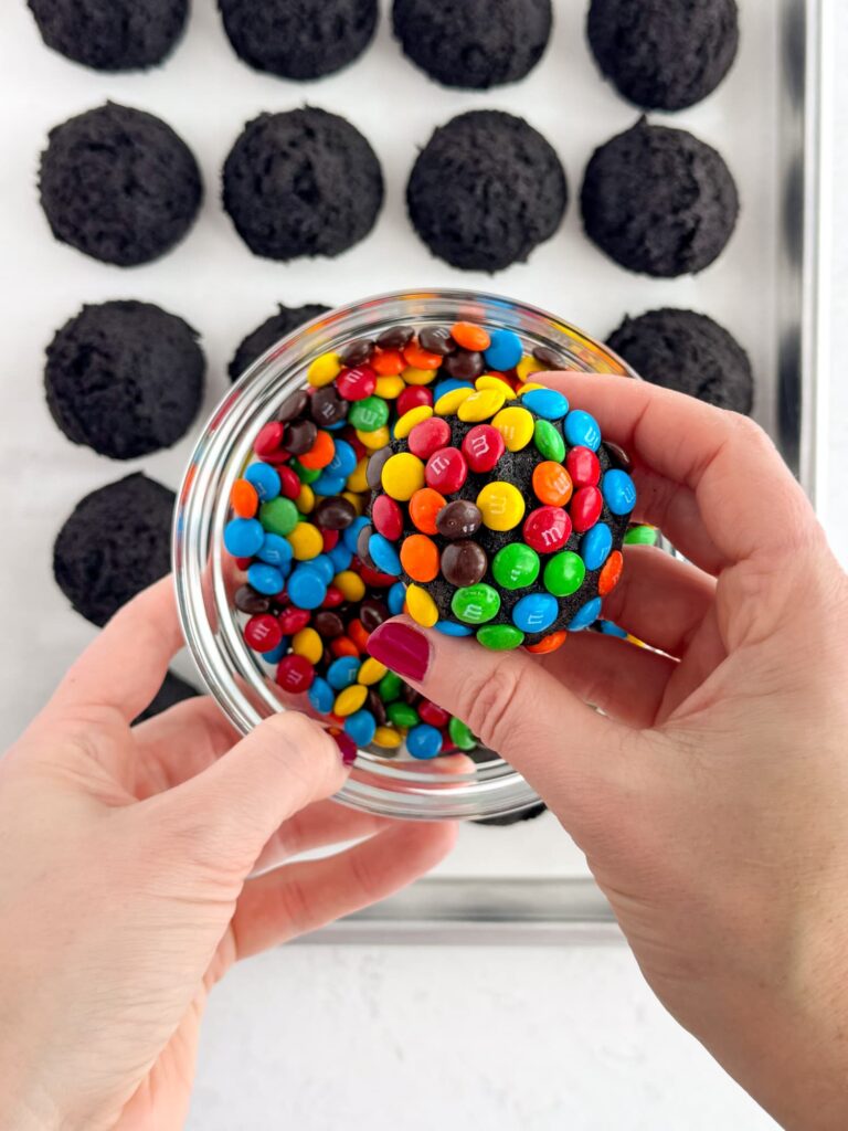 Rolling chocolate cookie dough balls in mini M&M candies.