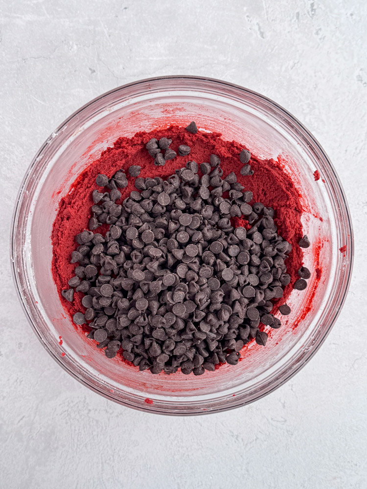 Red velvet cookie dough in a glass bowl with semisweet chocolate chips on the top.