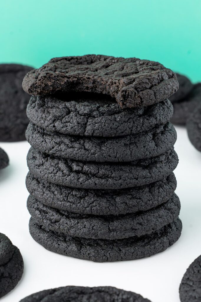 A stack of dark chocolate sugar cookies with a bite taken out of the top cookie to show the chewy interior texture.