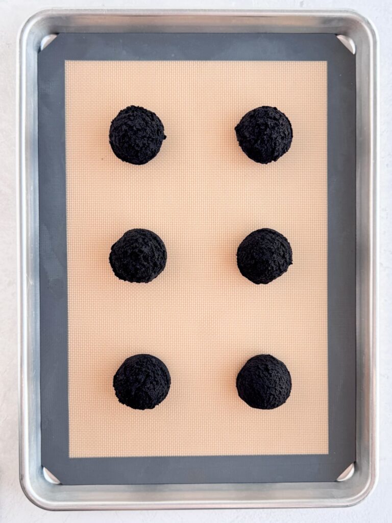 Dark chocolate cookie dough balls on a baking pan.