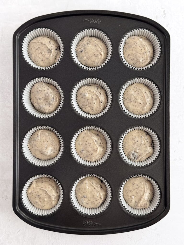 Vanilla Oreo cupcake batter in cupcake liners in a cupcake pan.