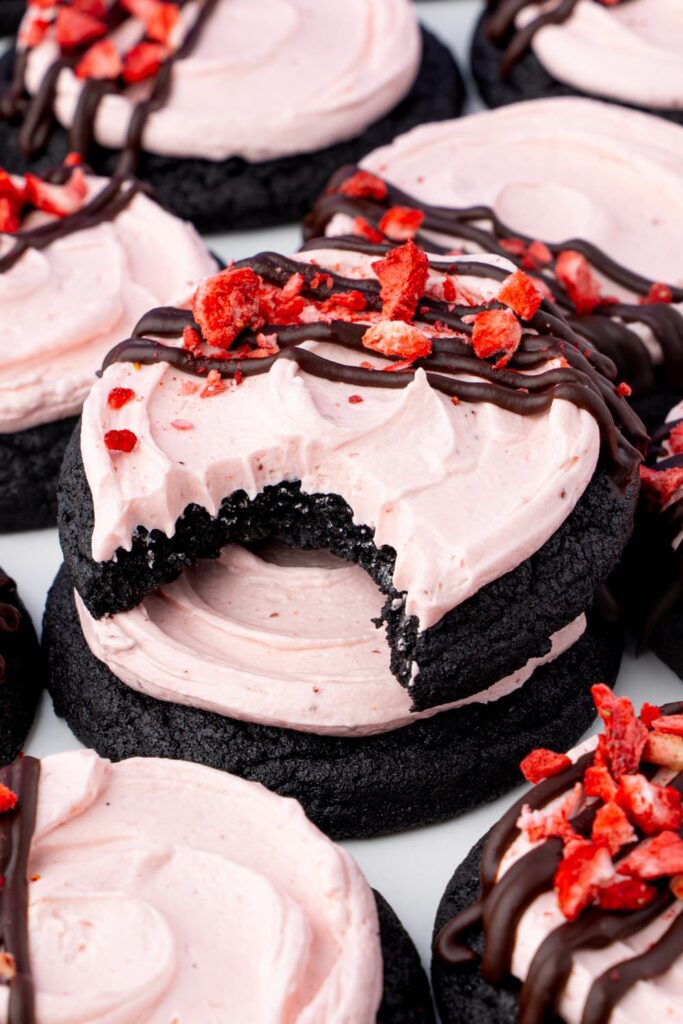 Strawberry frosted chocolate cookies with a bite taken out of the cookie to show the interior texture.