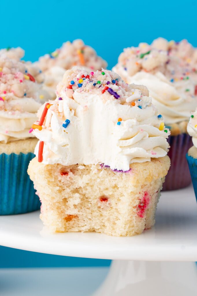 Birthday cake cupcake with a bite taken out to show the interior texture.