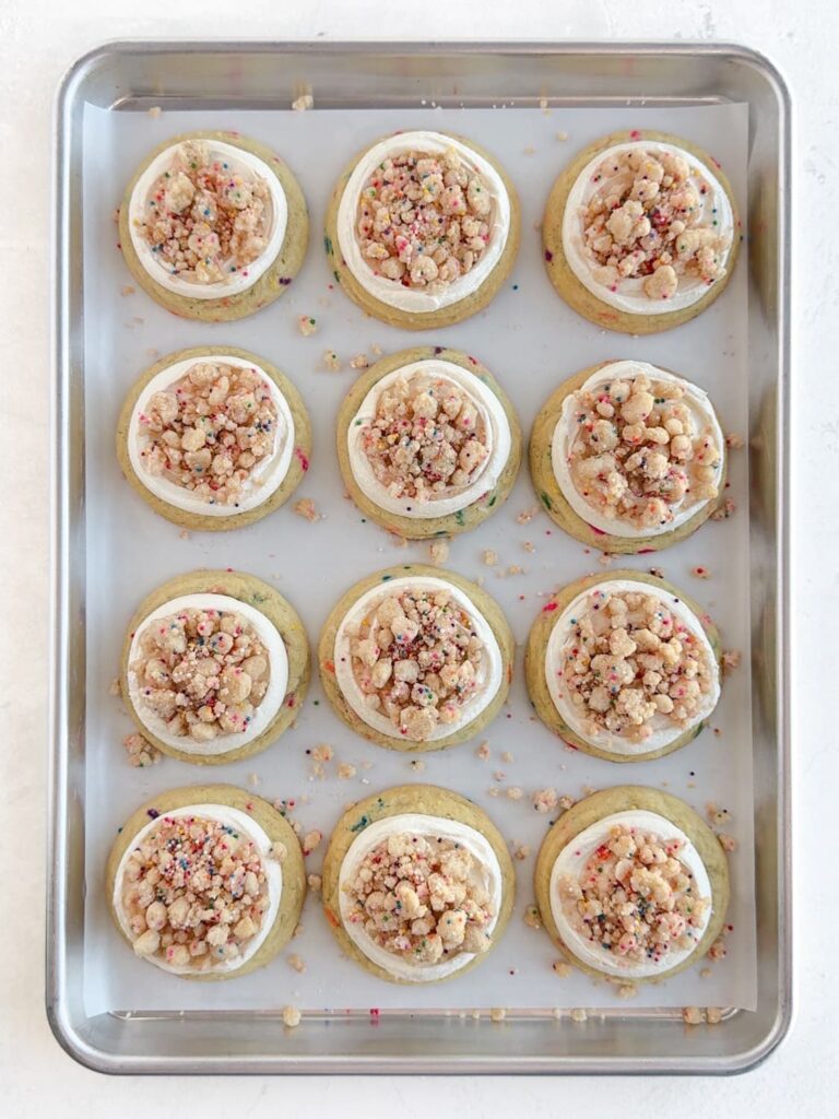 Sugar cookies topped with cake batter frosting and birthday cake crumbs.
