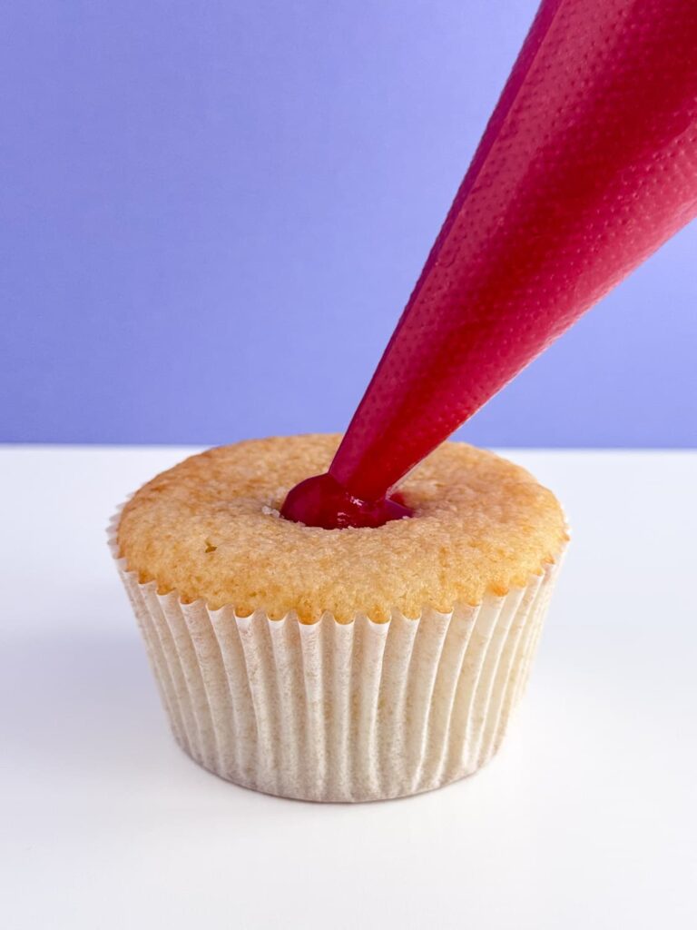 Filling a cupcake with raspberry filling.