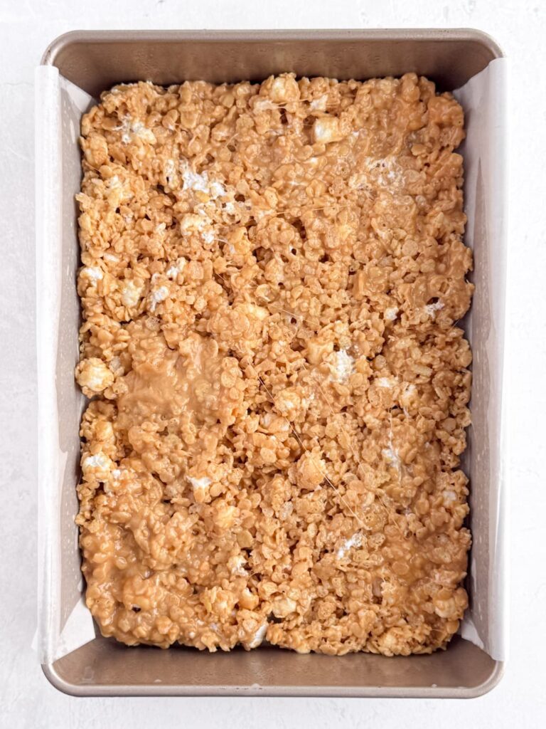 Peanut butter Rice Krispie treat mixture pressed into a baking pan.