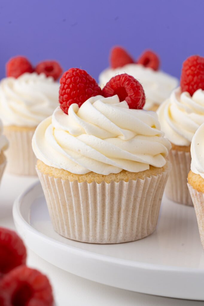 Vanilla almond cupcakes with raspberry filling and almond frosting on a plate.