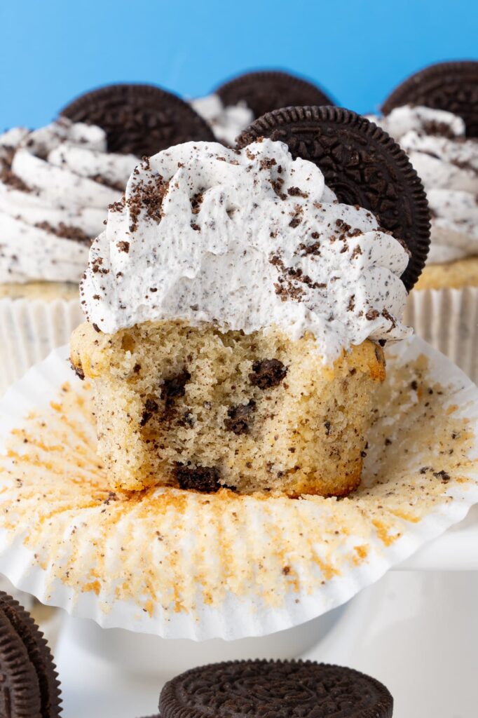 A cupcake with a bite taken out to show the interior texture of the vanilla cookies and cream cupcake.