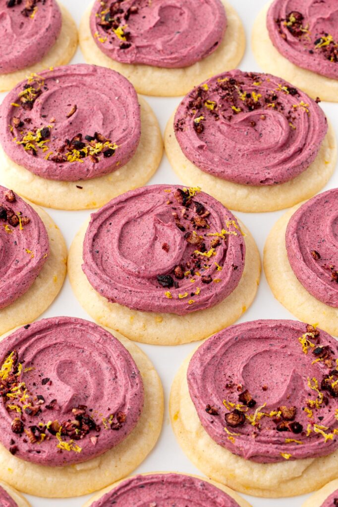 Soft lemon sugar cookies iced with blueberry buttercream and decorated with lemon zest.