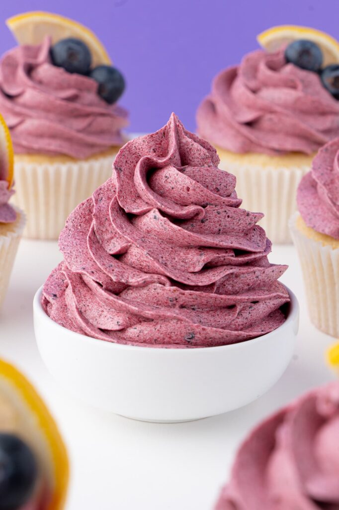 A swirl of blueberry buttercream frosting in a white bowl.