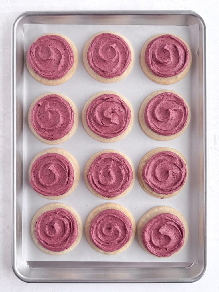 Lemon cookies frosted with blueberry buttercream on a baking sheet pan.