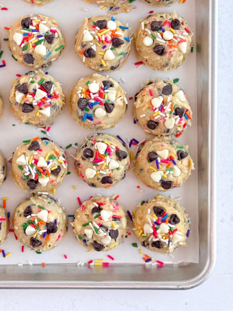 Scooped cake batter chocolate chip cookie dough on a baking sheet pan with additional chocolate chips and sprinkles pressed into the cookie dough.