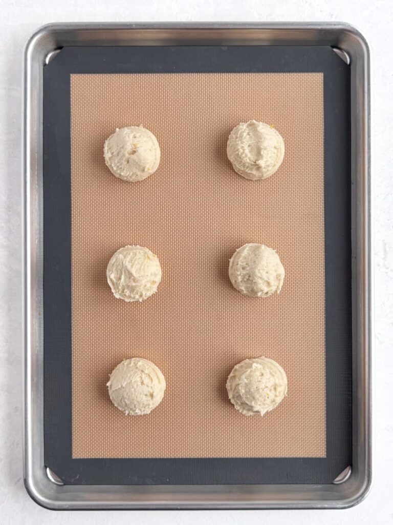 Lemon cookie dough balls on a prepared baking sheet pan.