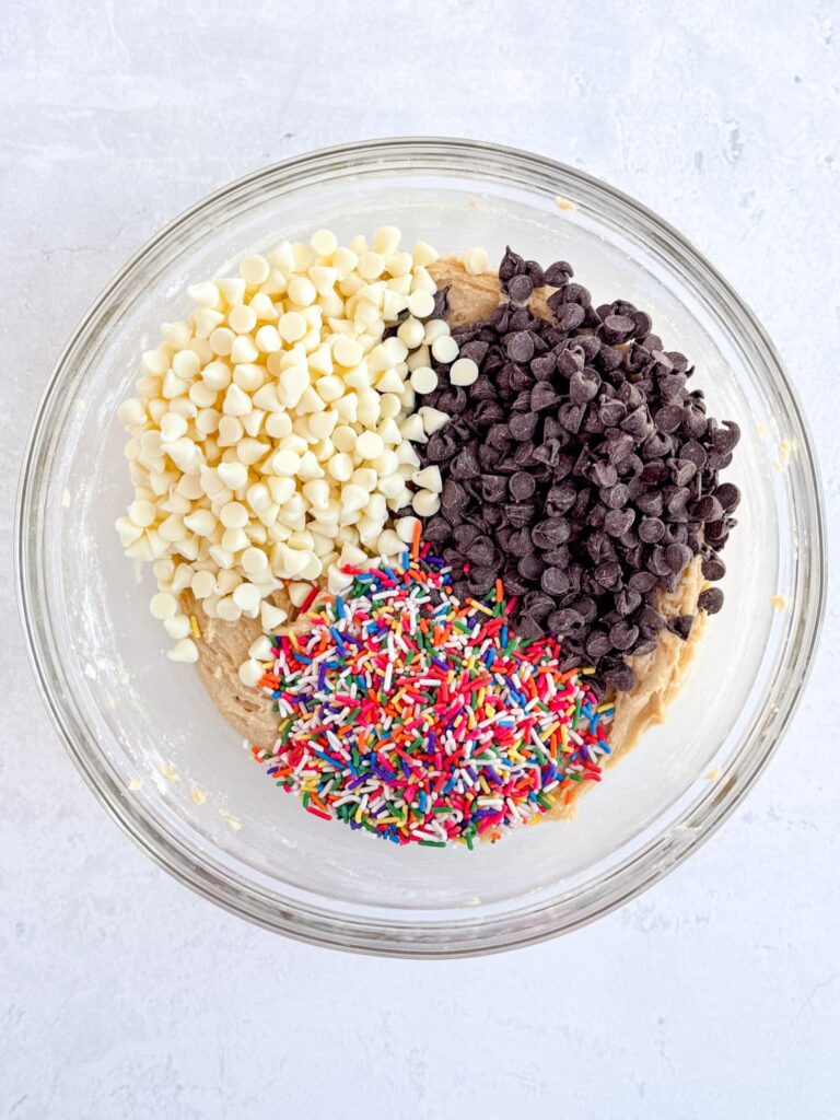 A bowl of cake batter cookie dough with semisweet chocolate, white chocolate, and rainbow sprinkles on top.