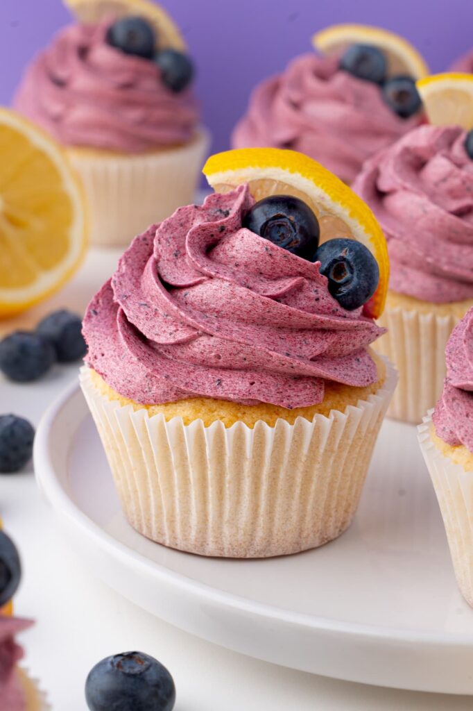 Soft lemon cupcakes with blueberry frosting, fresh blueberries, and lemon slices.