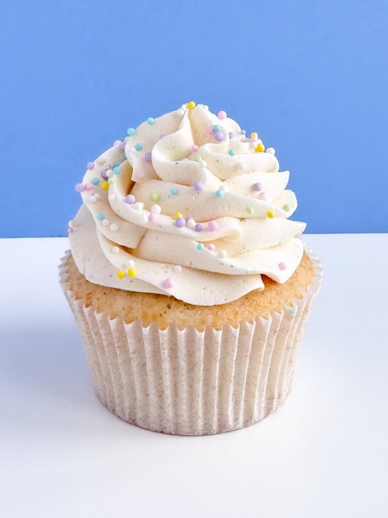 Vanilla cupcakes decorated with vanilla frosting an pastel nonpareil sprinkles.