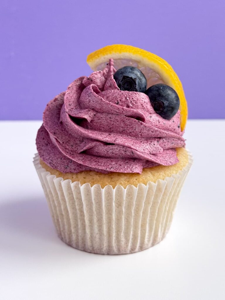 Blueberry frosted lemon cupcake with two blueberries and a lemon slice.