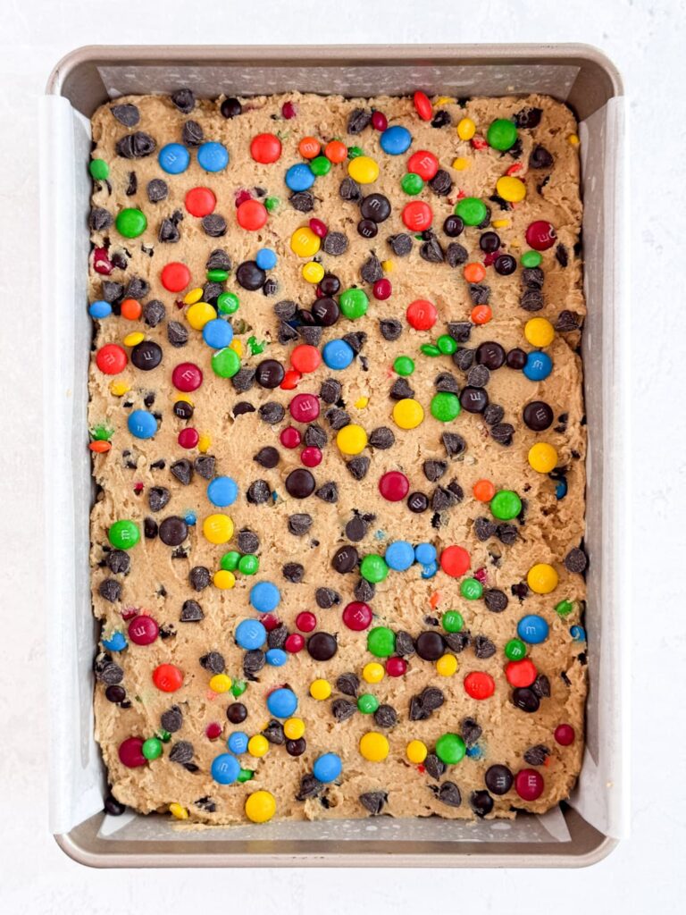 Extra semisweet chocolate chips and M&Ms on the peanut butter cookie dough in a baking pan.