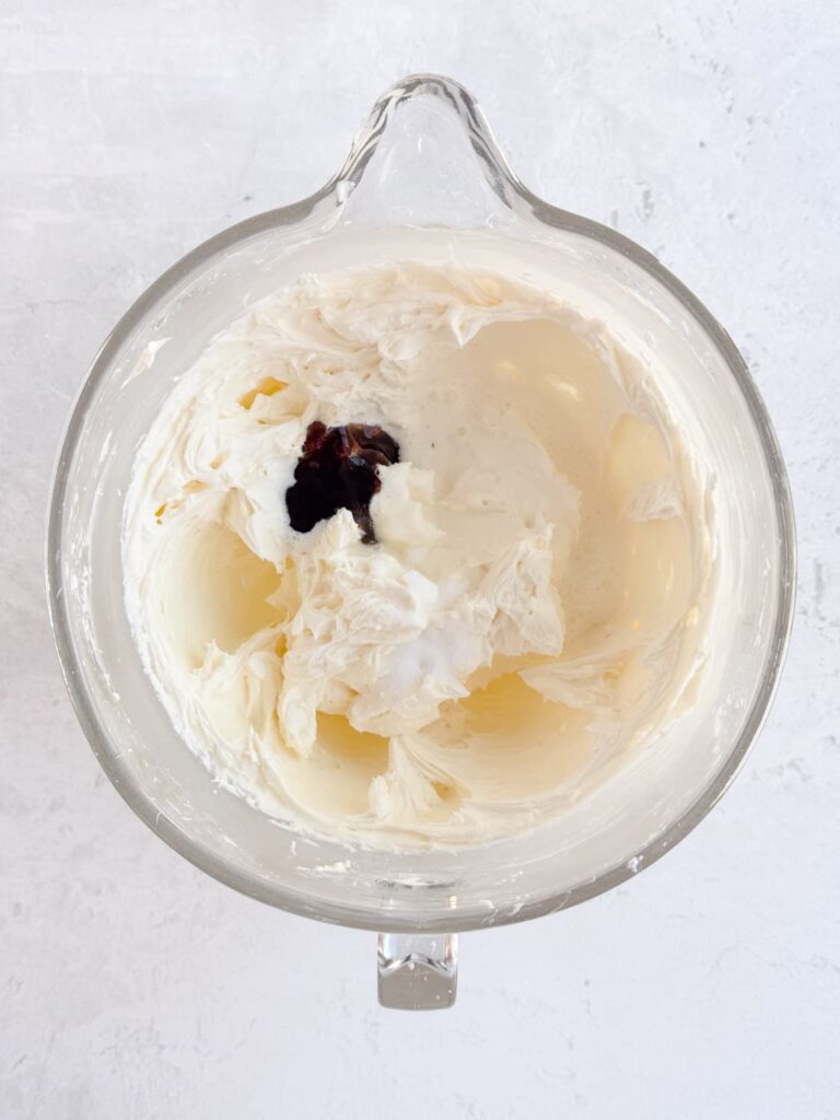 Heavy cream, vanilla bean paste, and salt added to the frosting in a mixing bowl.