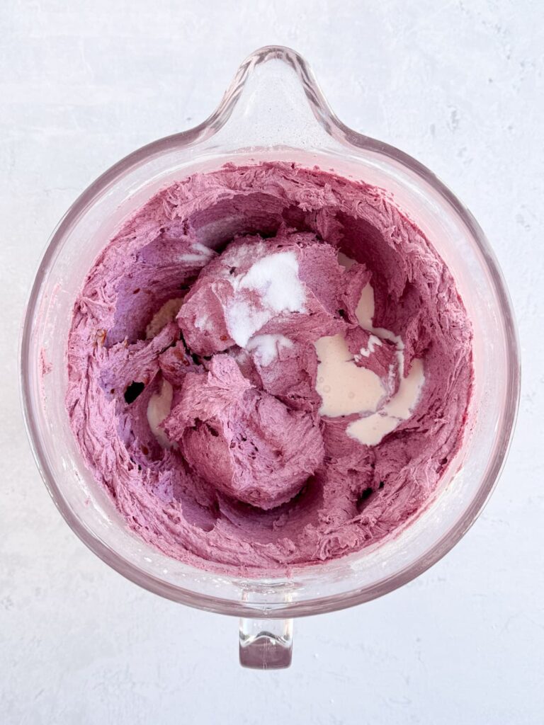 Heavy cream, vanilla, and salt added to frosting in a mixing bowl.