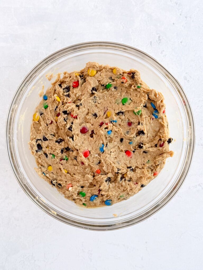 Peanut butter cookie dough with oats, chocolate chips, and M&Ms in a mixing bowl.