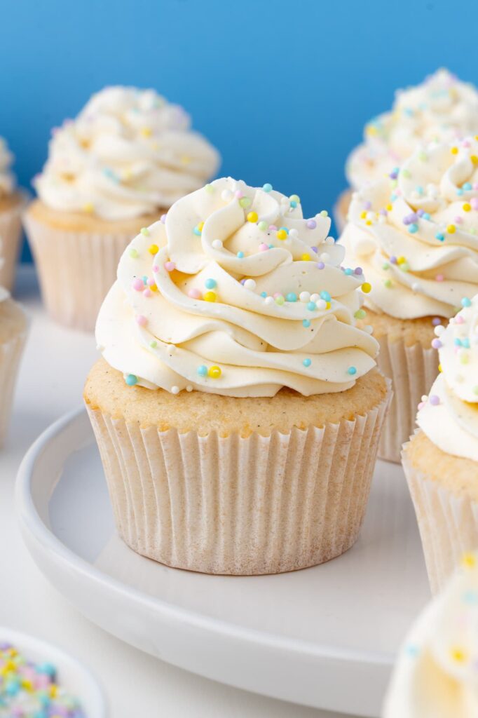 Vanilla cupcakes with vanilla frosting and sprinkles on a white plate.