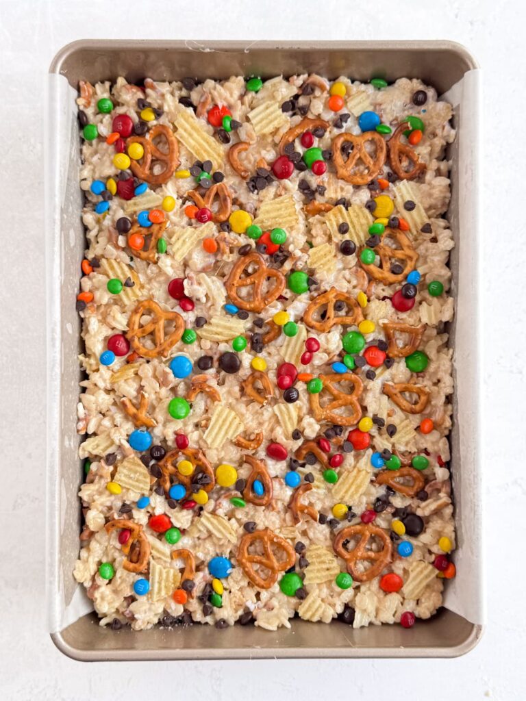 Rice Krispie treats with pretzels, potato chips, chocolate chips, and M&Ms in a baking pan.