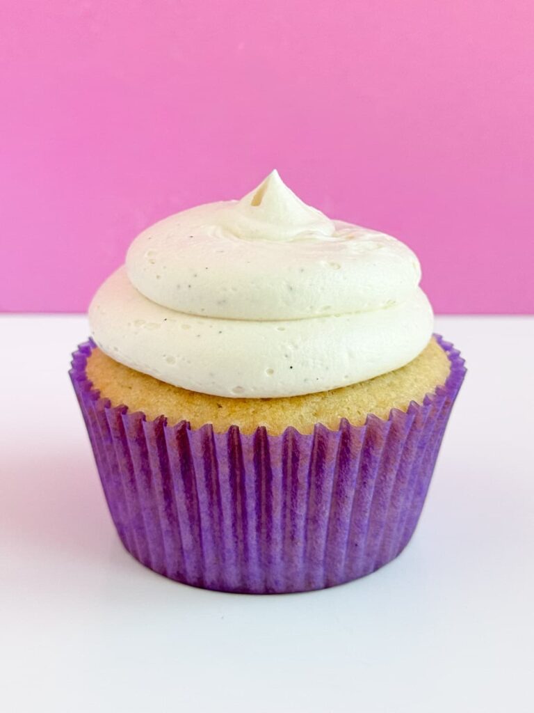 Vanilla cupcake in a purple cupcake liner with vanilla buttercream piped on top.