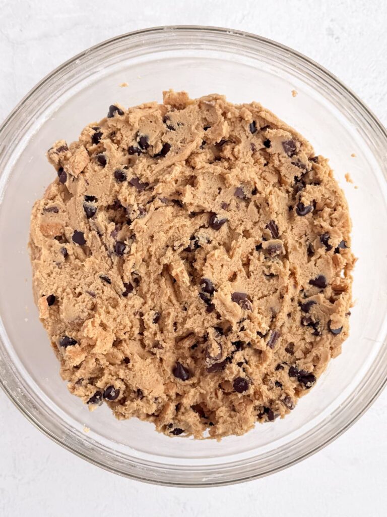 Peanut butter cookie dough with graham crackers and chocolate chips in a mixing bowl.
