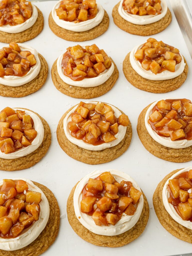Frosted caramel apple cookies topped with cinnamon apples, homemade salted caramel sauce, and flaky sea salt.